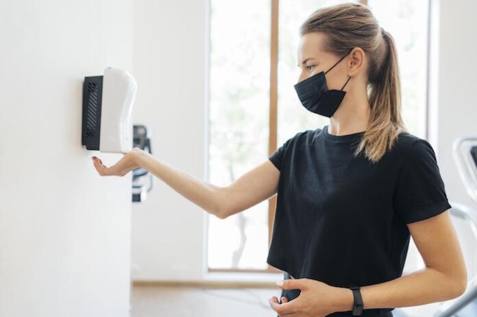 side-view-woman-with-medical-mask-disinfecting-her-hands-gym
