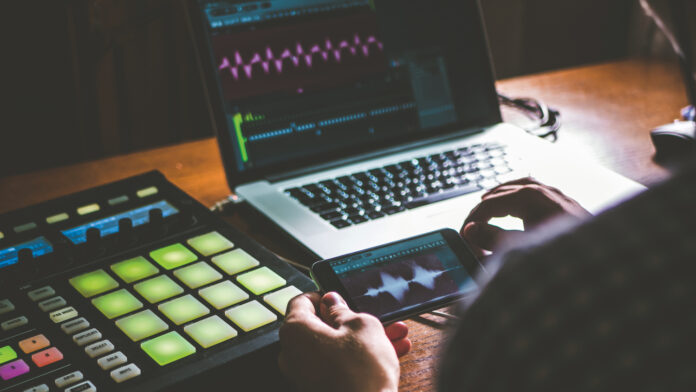 close up person creating music using phone and other sound equipment with laptop